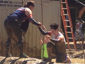Runner helping another running, via hands clasps, get out of a hole after an obstacle. 